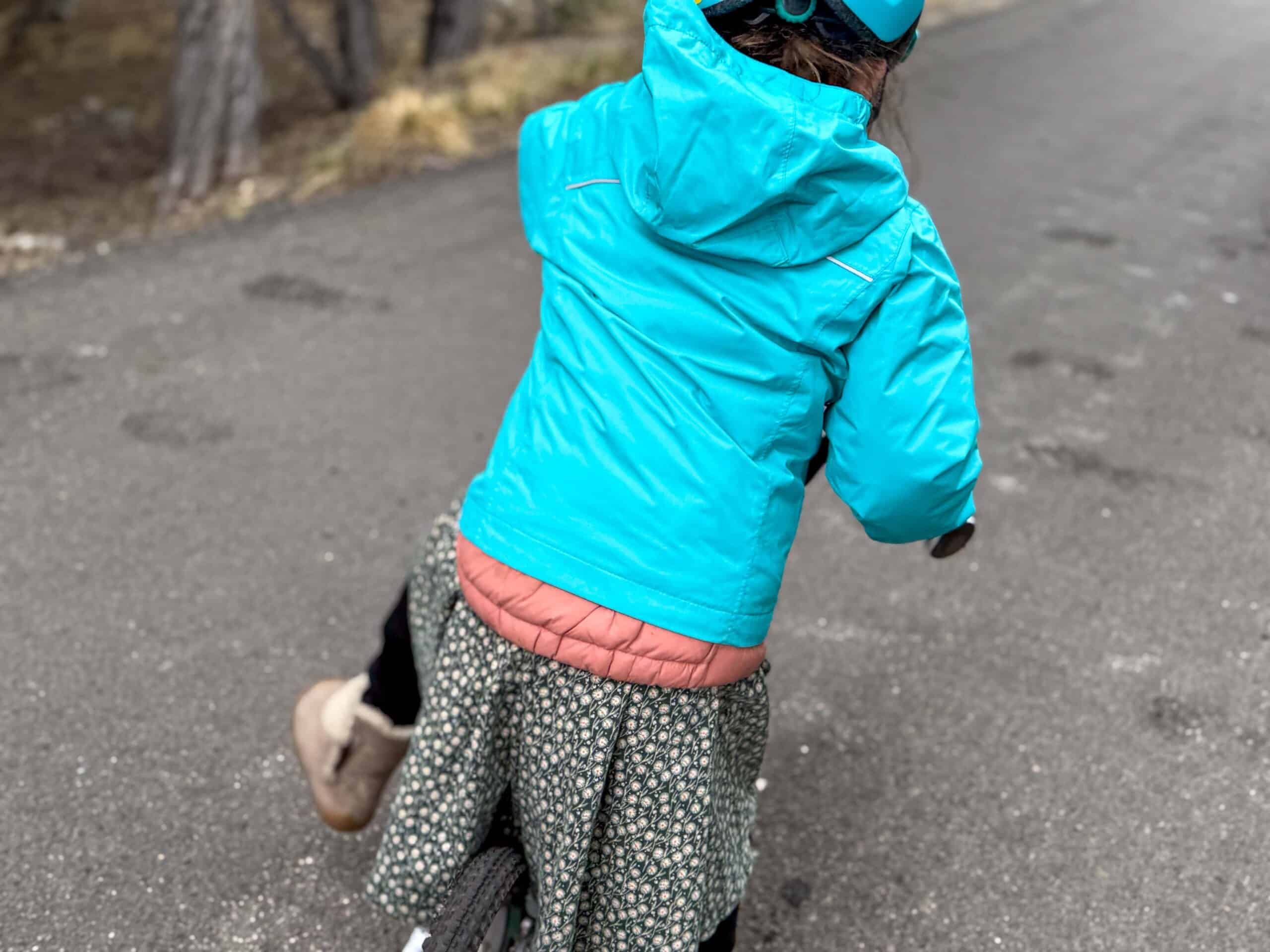 little girl in bright blue jacket riding a bike
