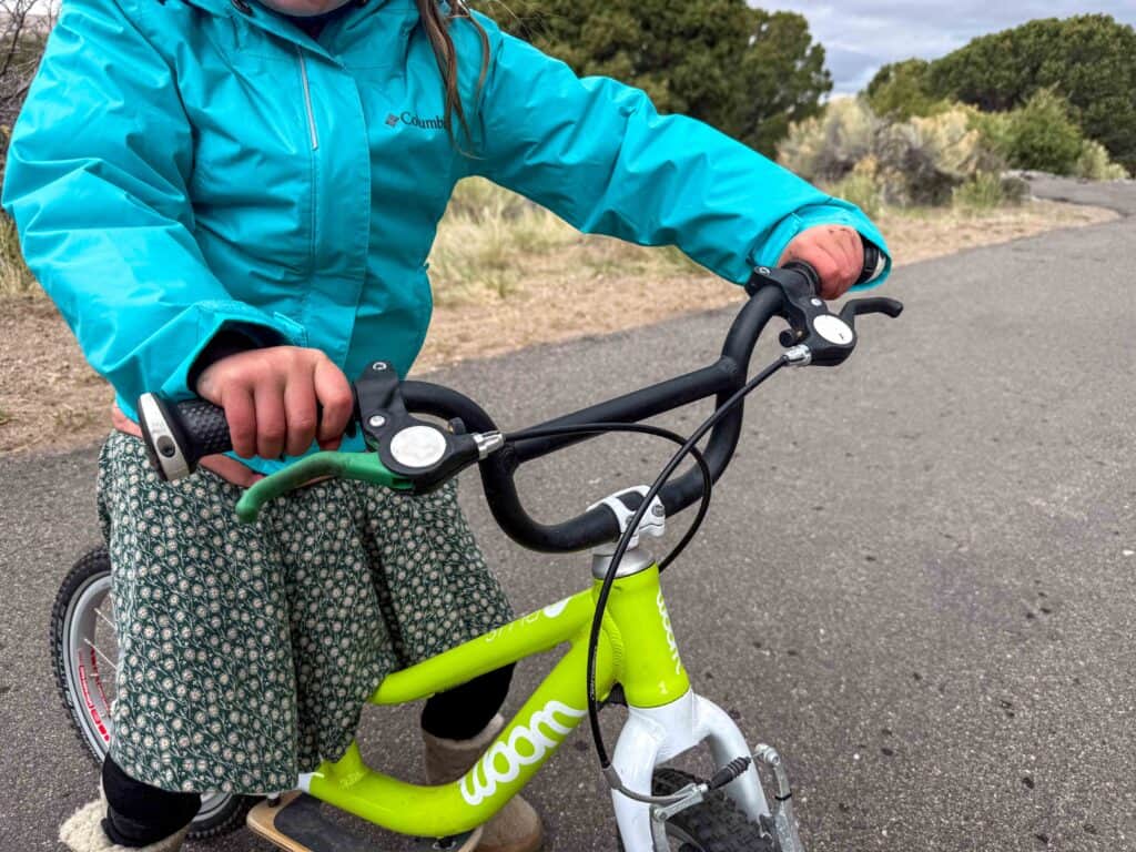 Child riding green Woom bike on outdoor paved path