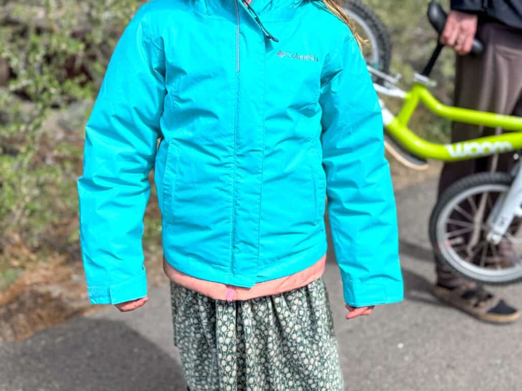 Child in teal Columbia jacket with bike in background