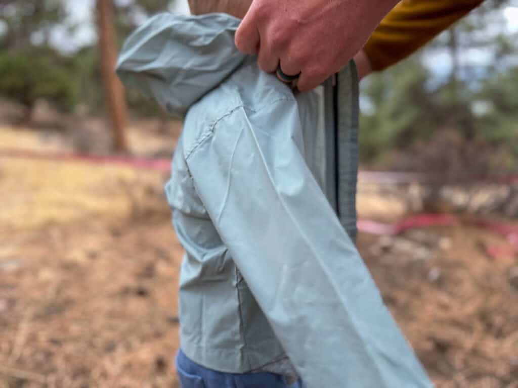 Person holding lightweight rain jacket outdoors in wooded area