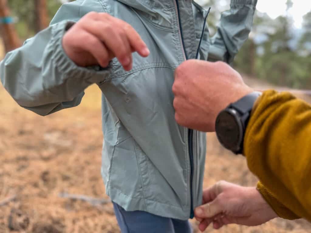 a man zipa up a little boys jacket in a field