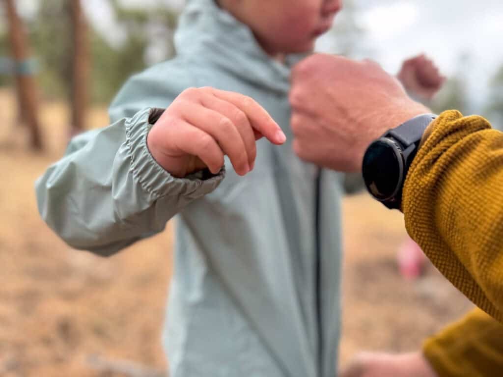 Adult helping child zip up rain jacket outdoors