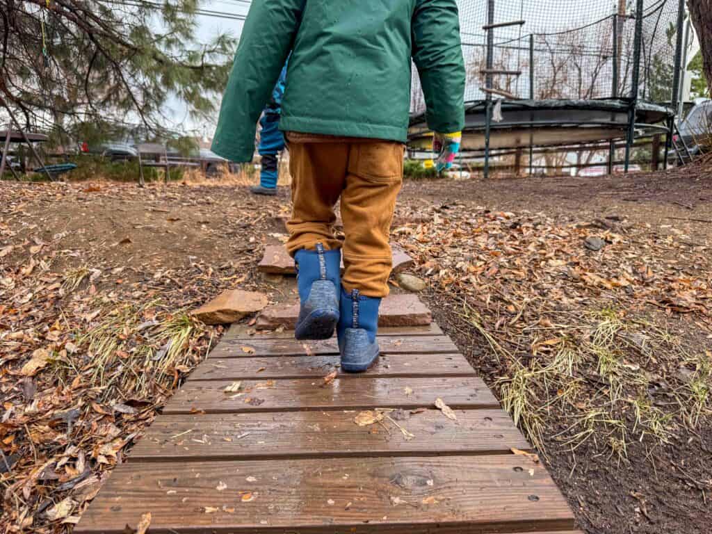 Child in rain boots walking on wet wooden path outdoors
