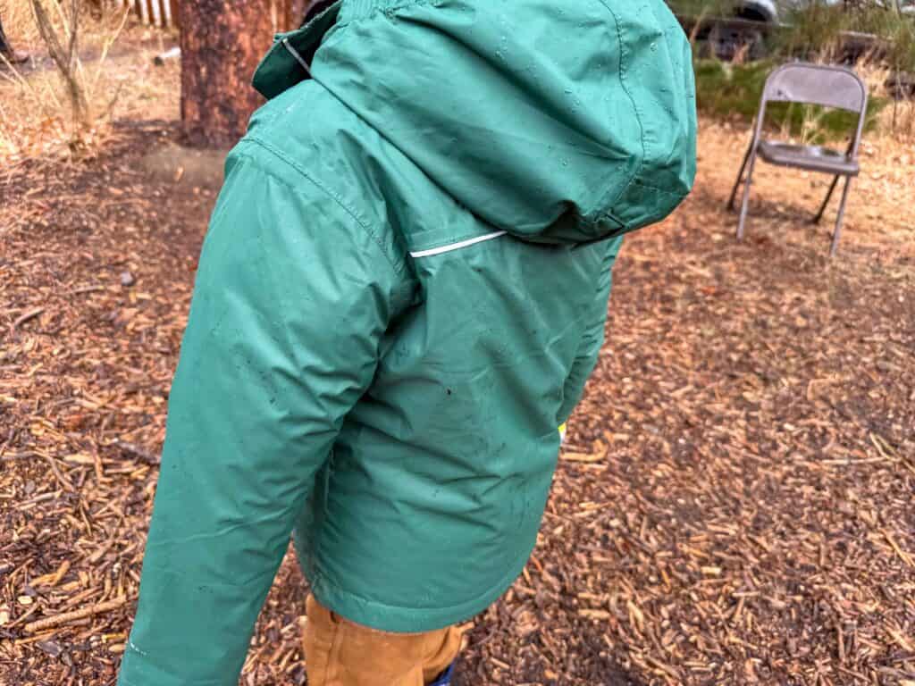Person wearing wet green rain jacket outdoors in wooded area