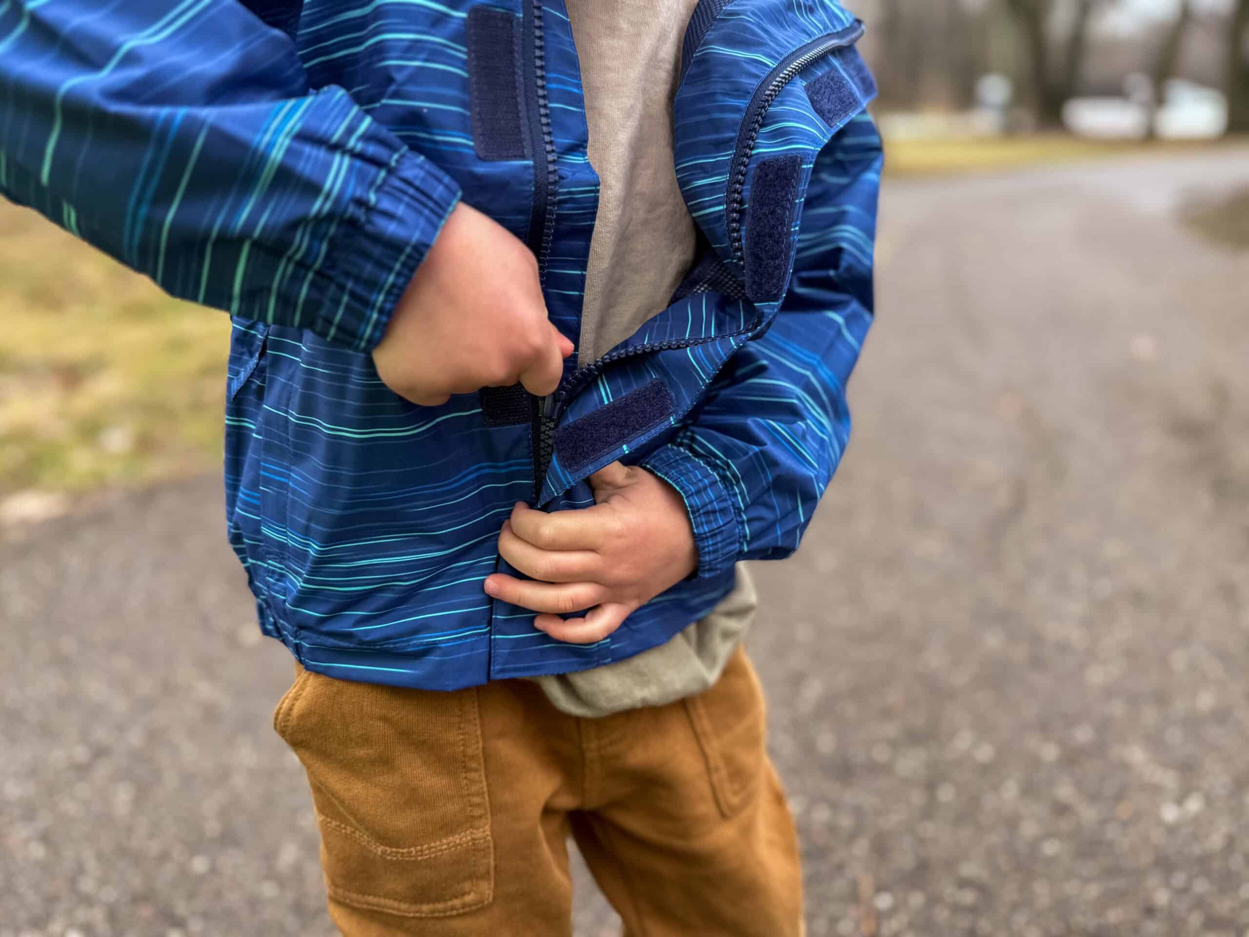 kids zips up blue jacket on pavement