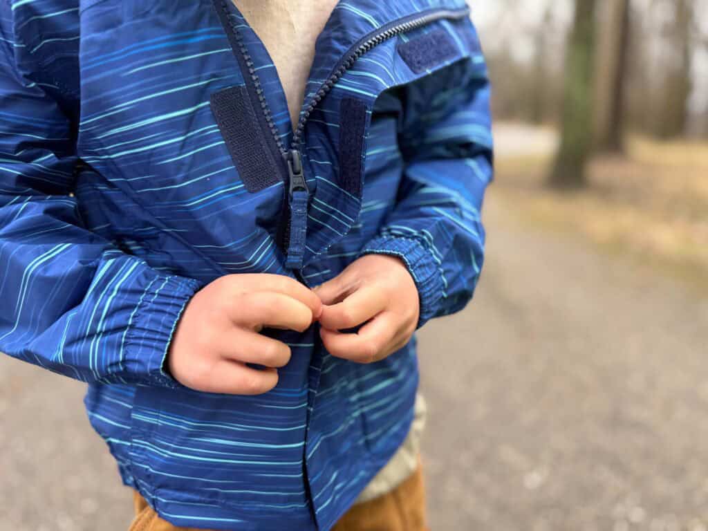 Child zipping up blue striped windbreaker jacket outdoors