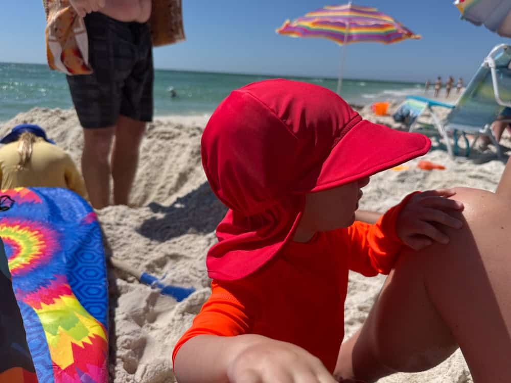 Toddler in red sun hat and swimsuit at beach