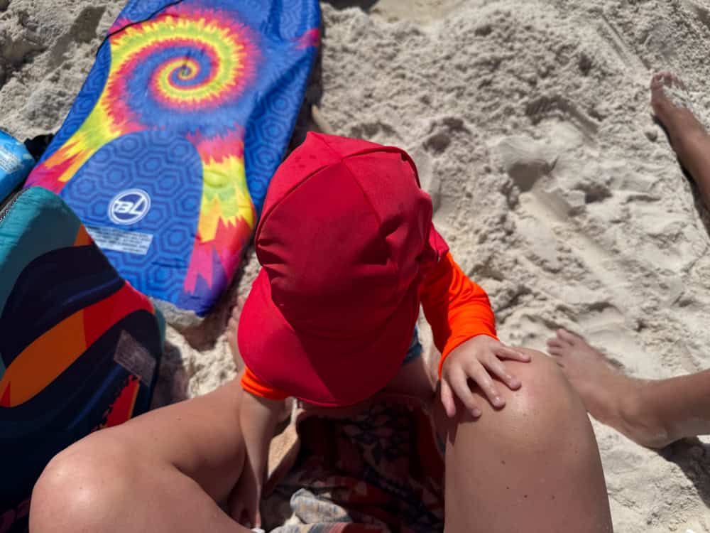 Baby in red sun hat playing on sandy beach
