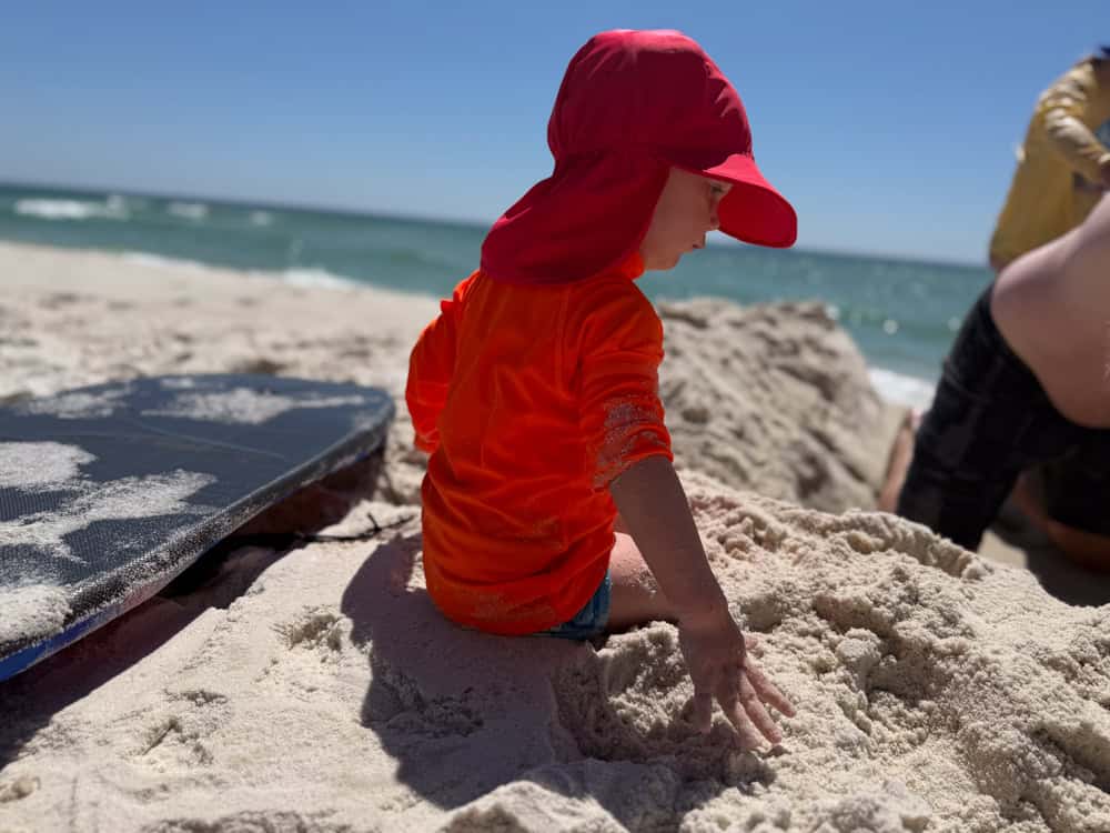 Young child in red hat playing in beach sand