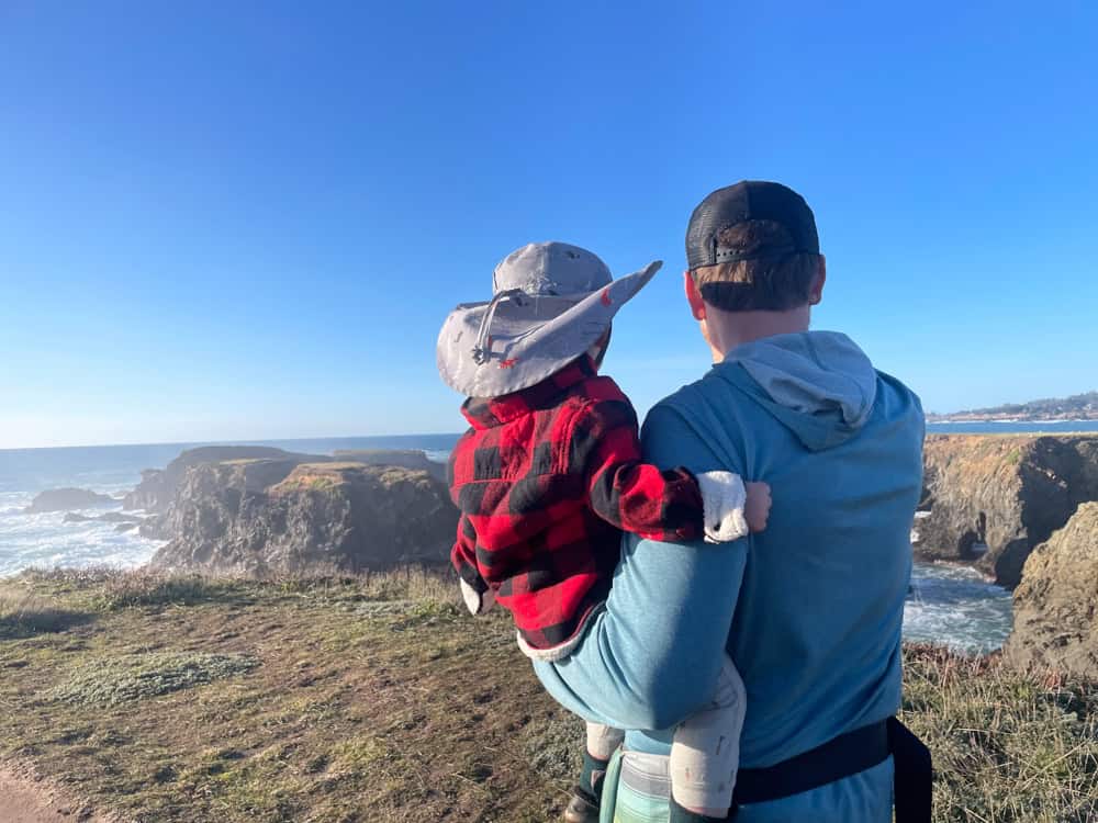 Father holding young child overlooking rugged coastal cliffs