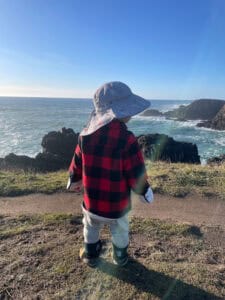 Toddler in plaid jacket gazing at rocky ocean coastline