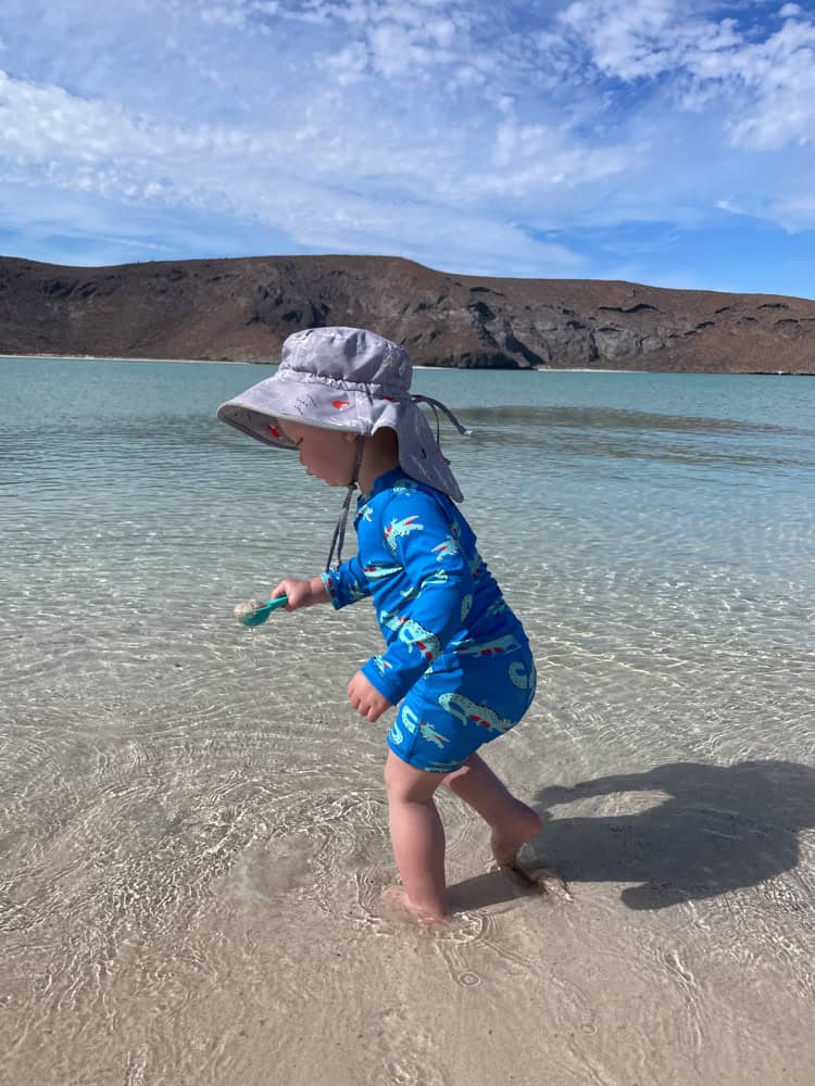 Toddler in blue swimsuit playing in shallow beach water