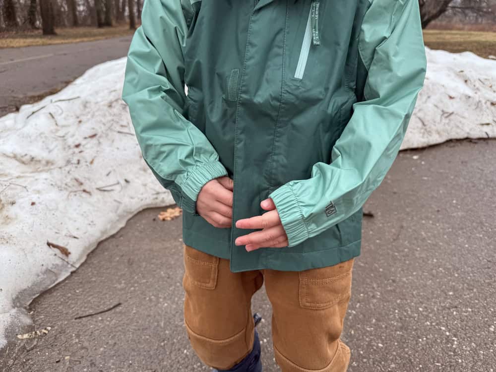 Child wearing green rain jacket outdoors near melting snow