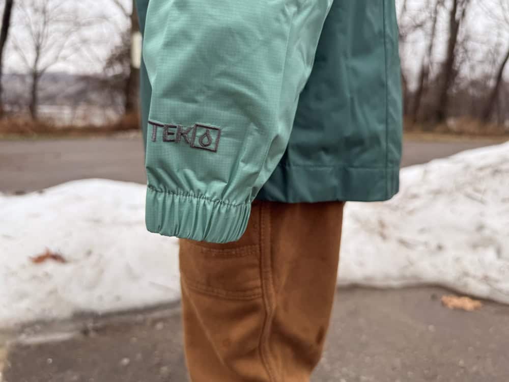 boy in rain jacket with long sleeves with snow behind