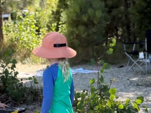Young child in sun hat exploring a wooded campsite