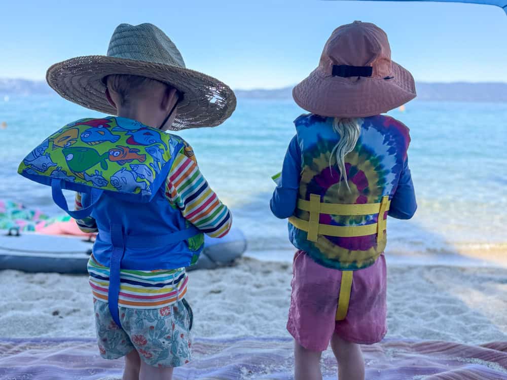 Two young children in life vests gazing at the beach