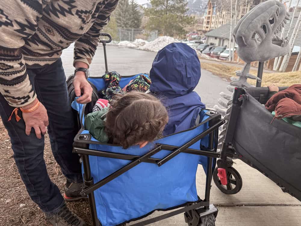 two kids sit in a blue wagon on their way to a music festival in the rain