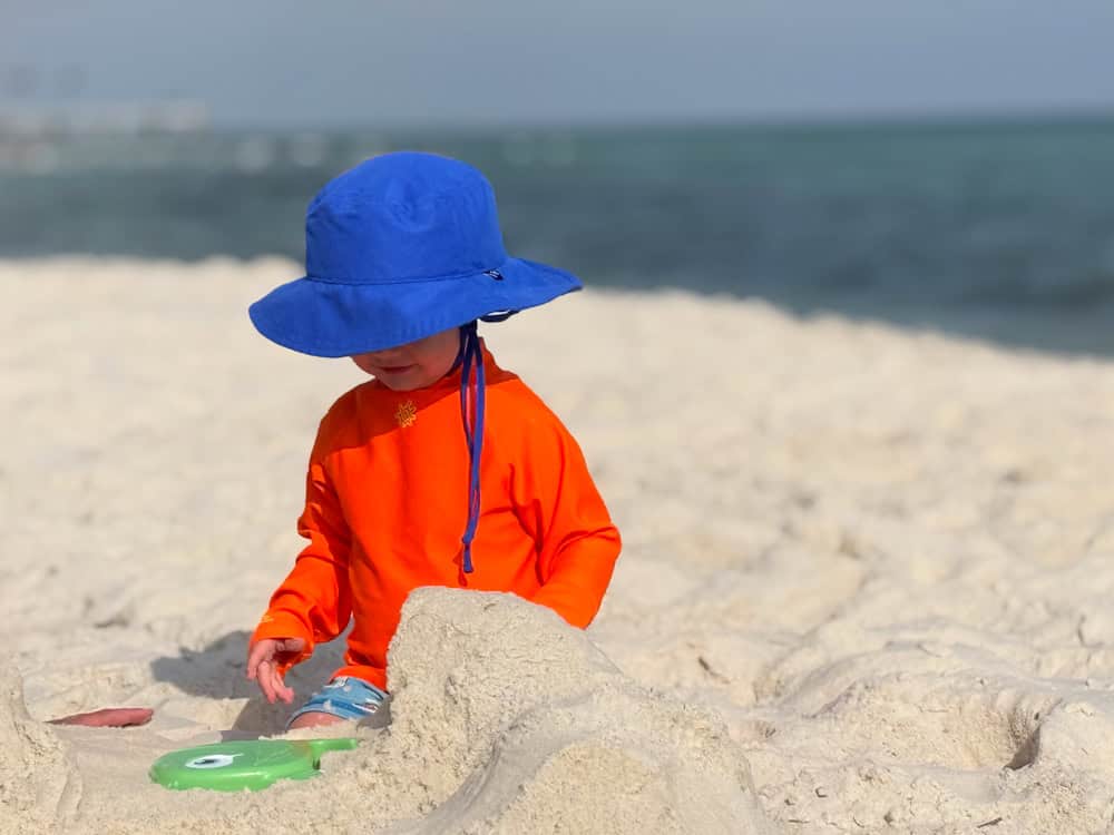 Young child in blue hat playing in beach sand