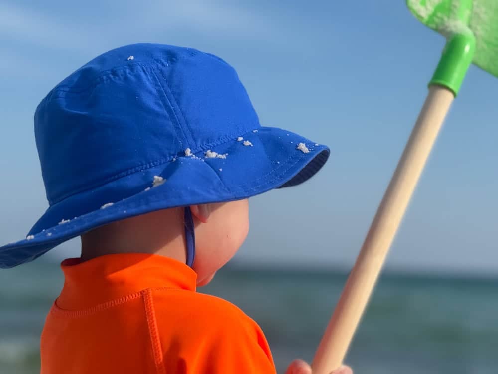 Young child with blue hat holding green net at beach