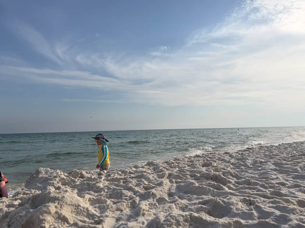 Child in hat walking on white sand beach by ocean