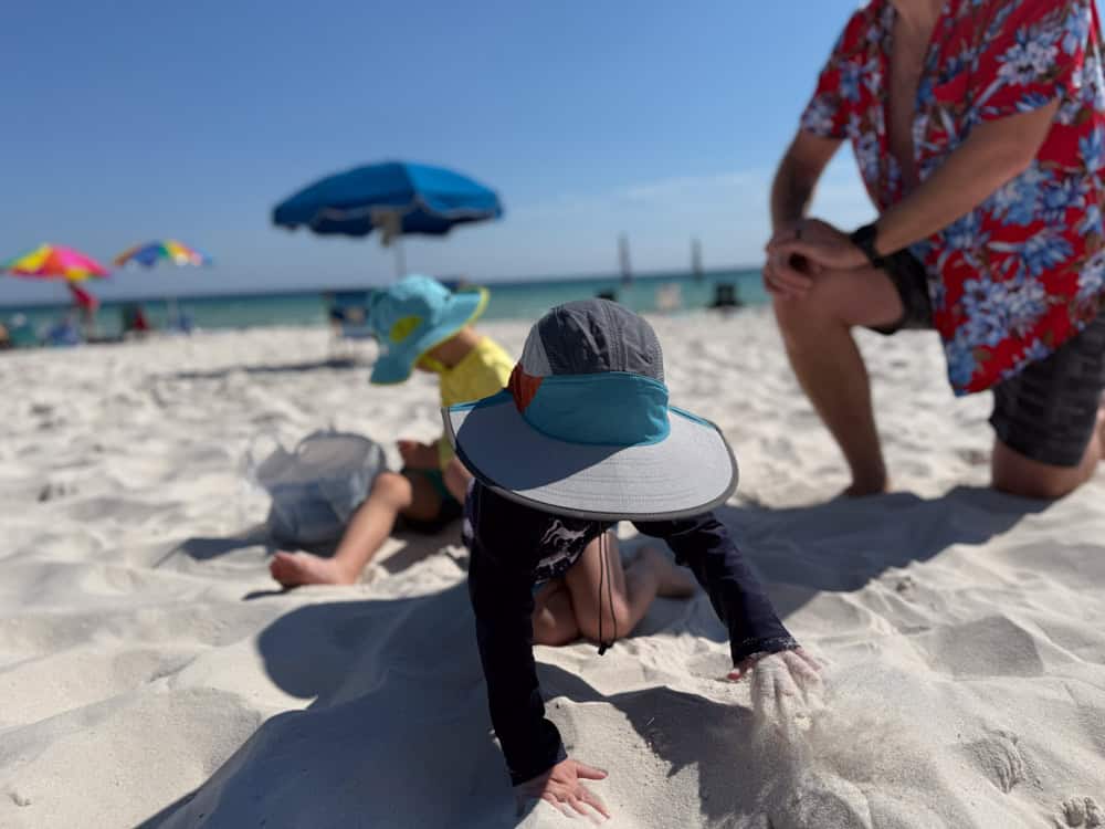 Baby crawling on white sand beach with family nearby