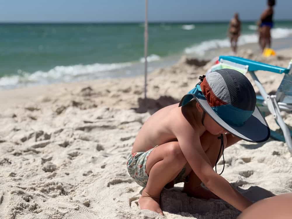 Toddler in sun hat playing in sand at beach