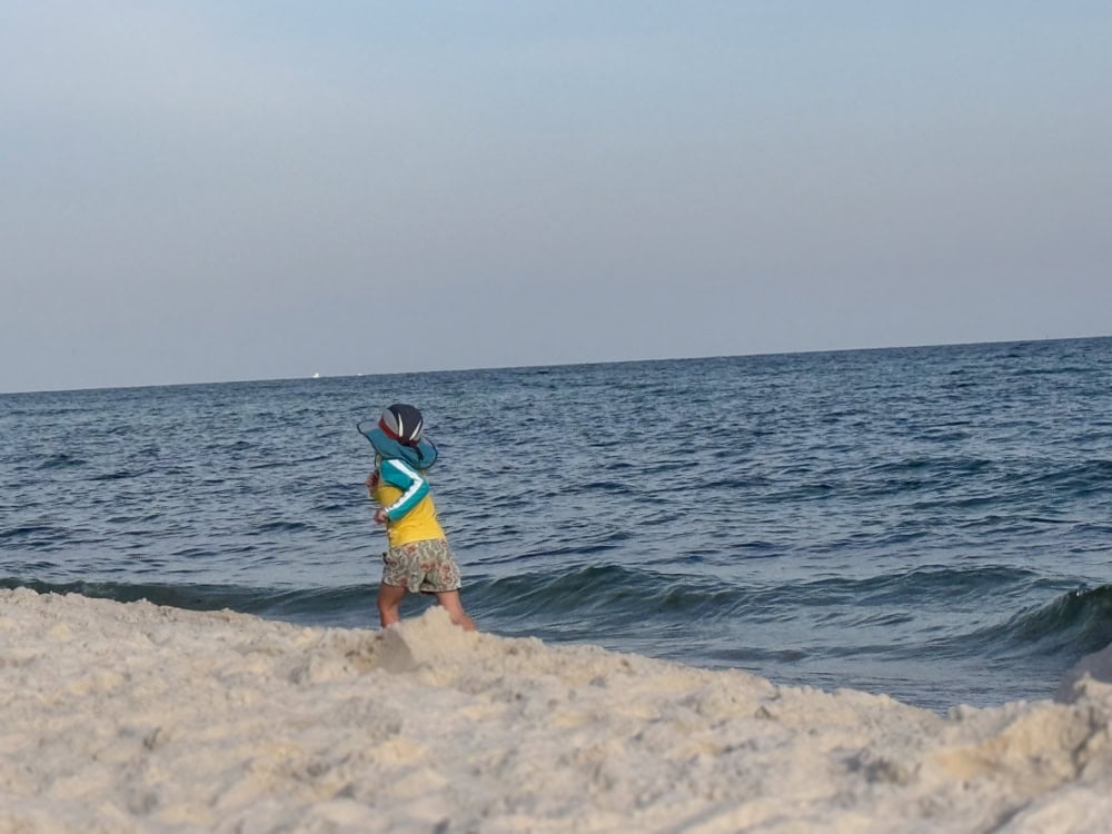 Young child in hat playing at ocean shoreline