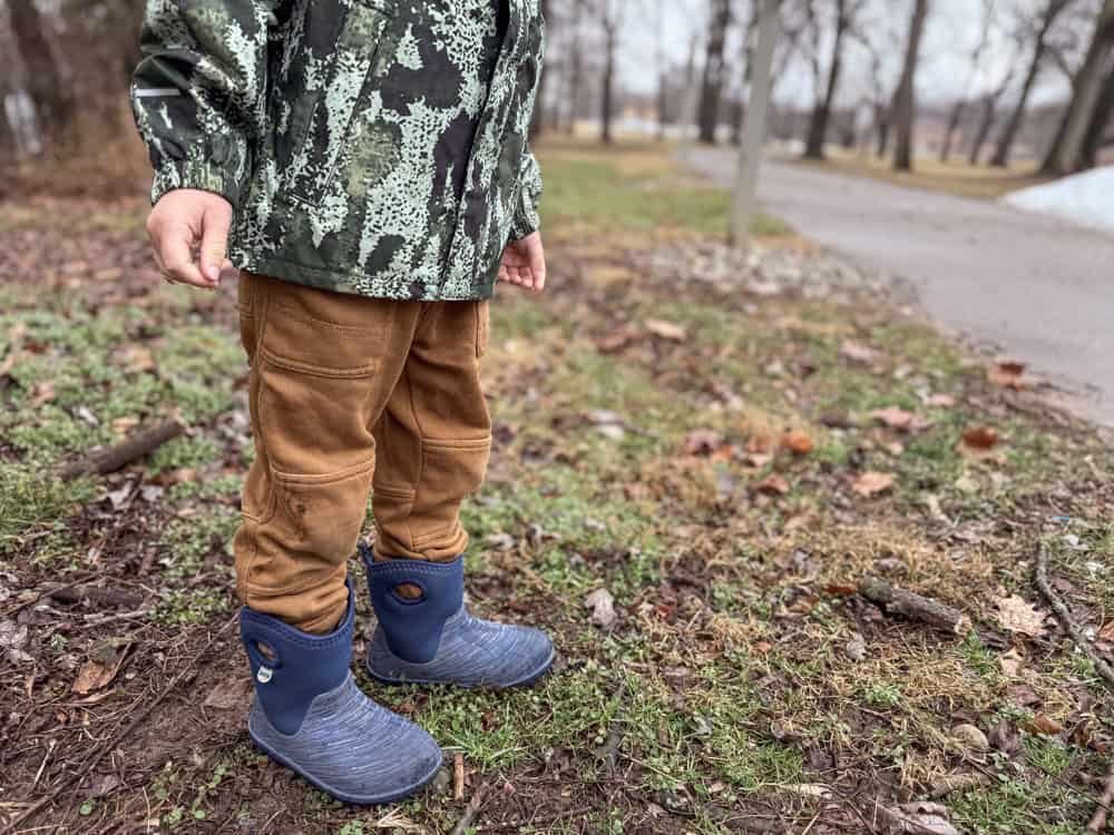 Toddler in camo jacket and blue rain boots outdoors