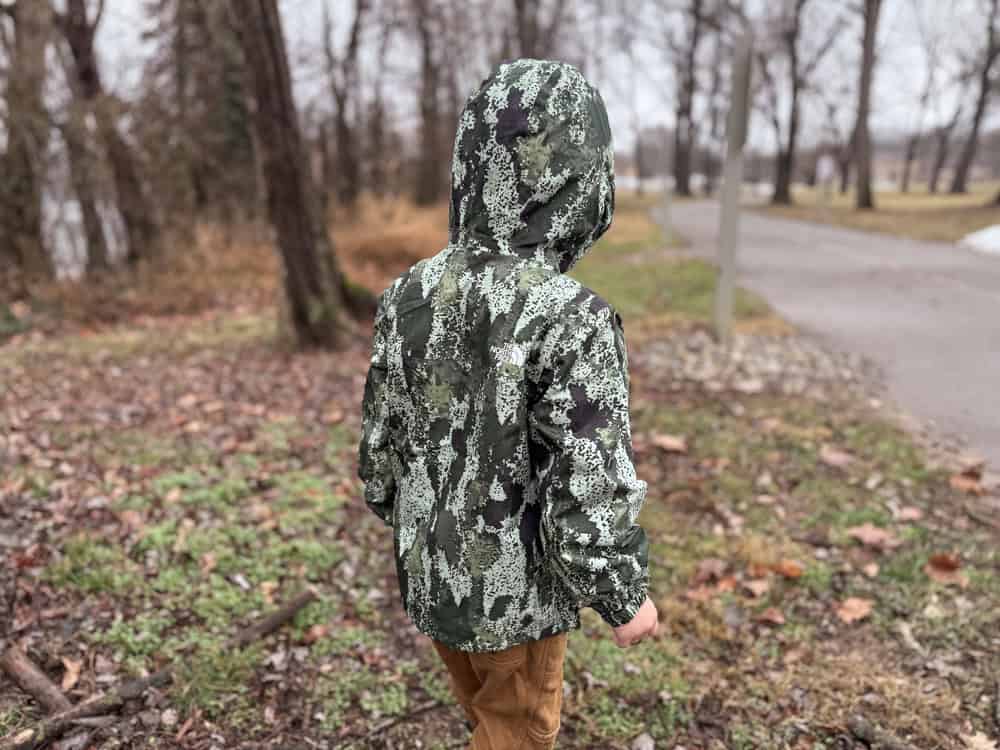 a boy in a camoflauged rain jacket walks toward a path in the rain