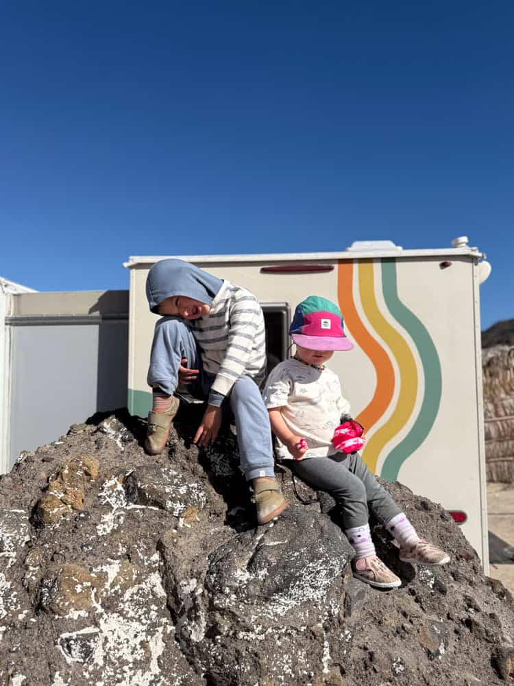 Two young children sitting on a large rock near an RV