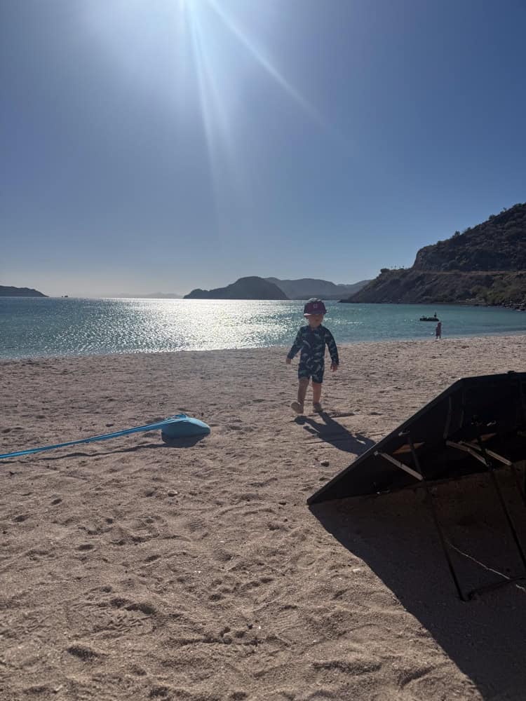 Toddler walking on sunny beach with calm blue water