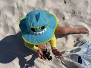 Toddler in shark hat playing with toy truck on beach