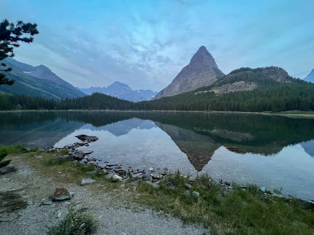 Calm mountain lake reflecting sharp rocky peak at dusk