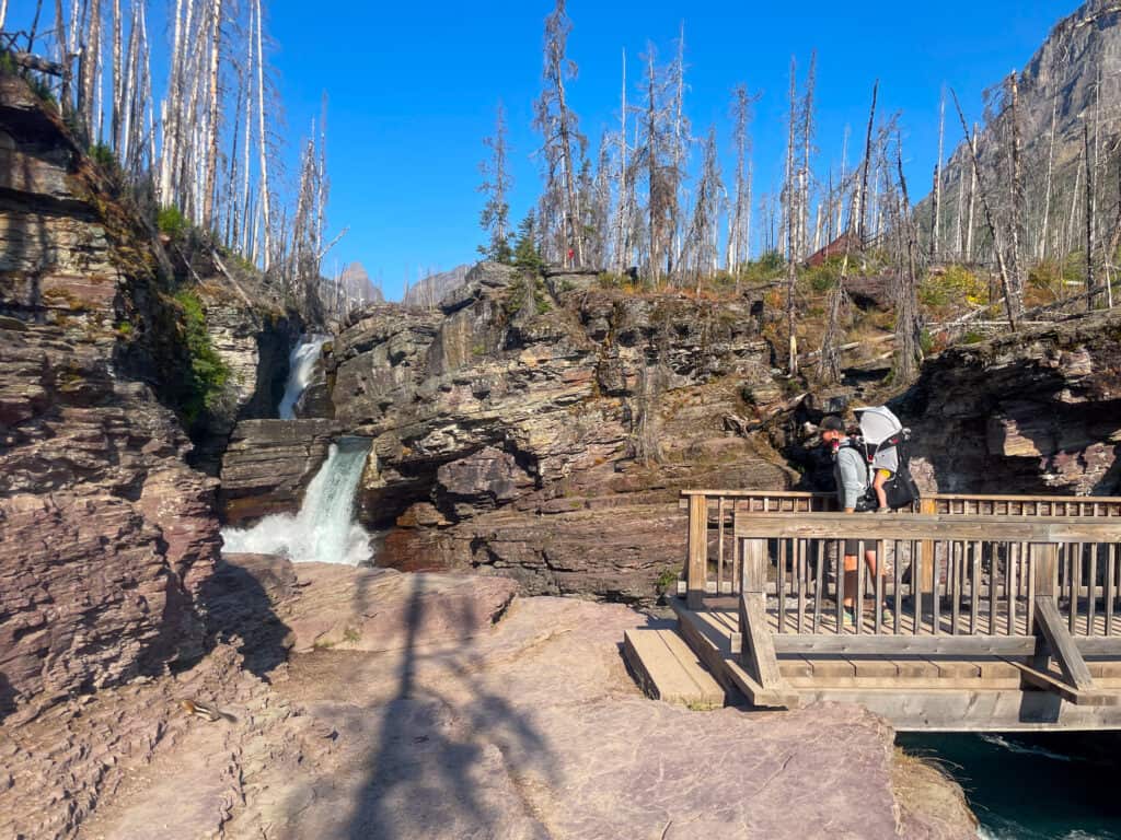 Hiker with baby carrier on wooden deck near mountain waterfall