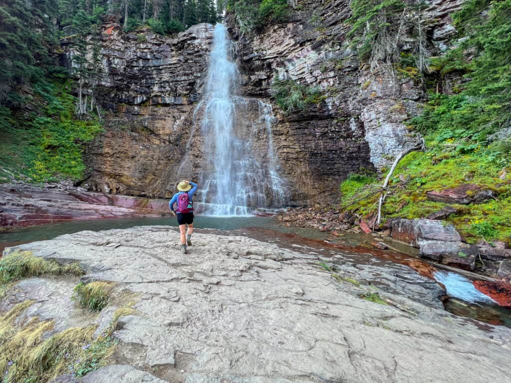 Hiker with backpack approaching tall waterfall on rocky terrain
