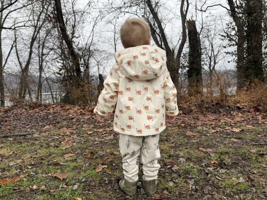 Full length back view of toddler in Amazon Essentials Toddler Rain Jacket standing in leaf-covered outdoor setting