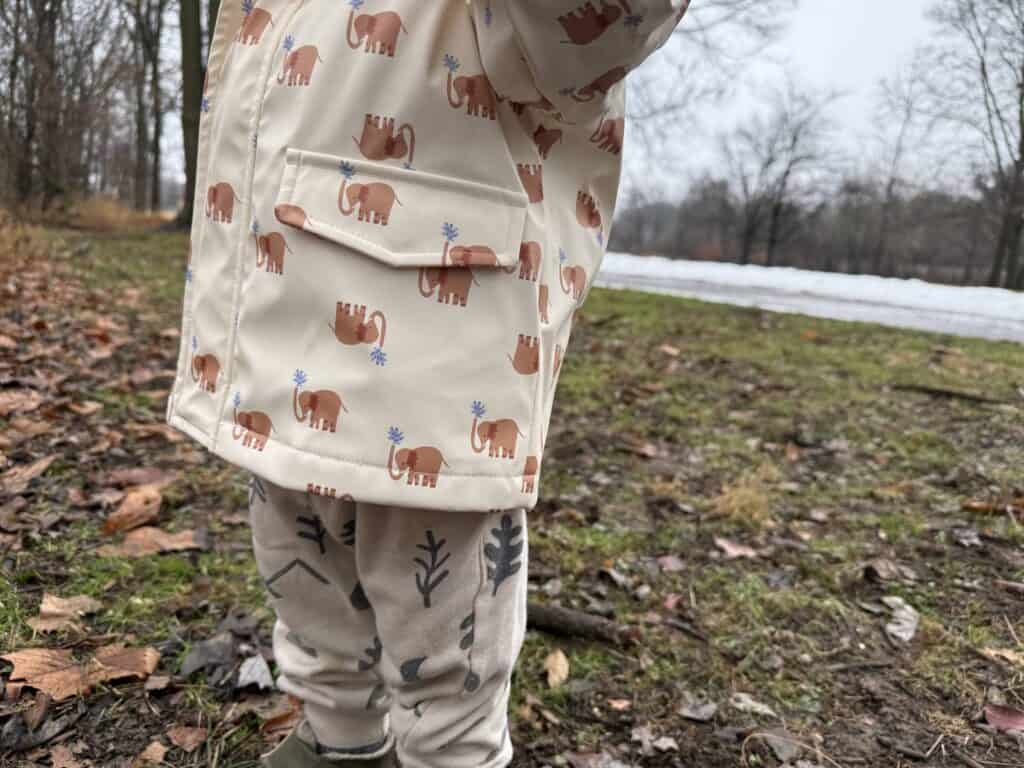 Front torso view of toddler in Amazon Essentials Toddler Rain Jacket with hood up showing welt pockets and snap guard