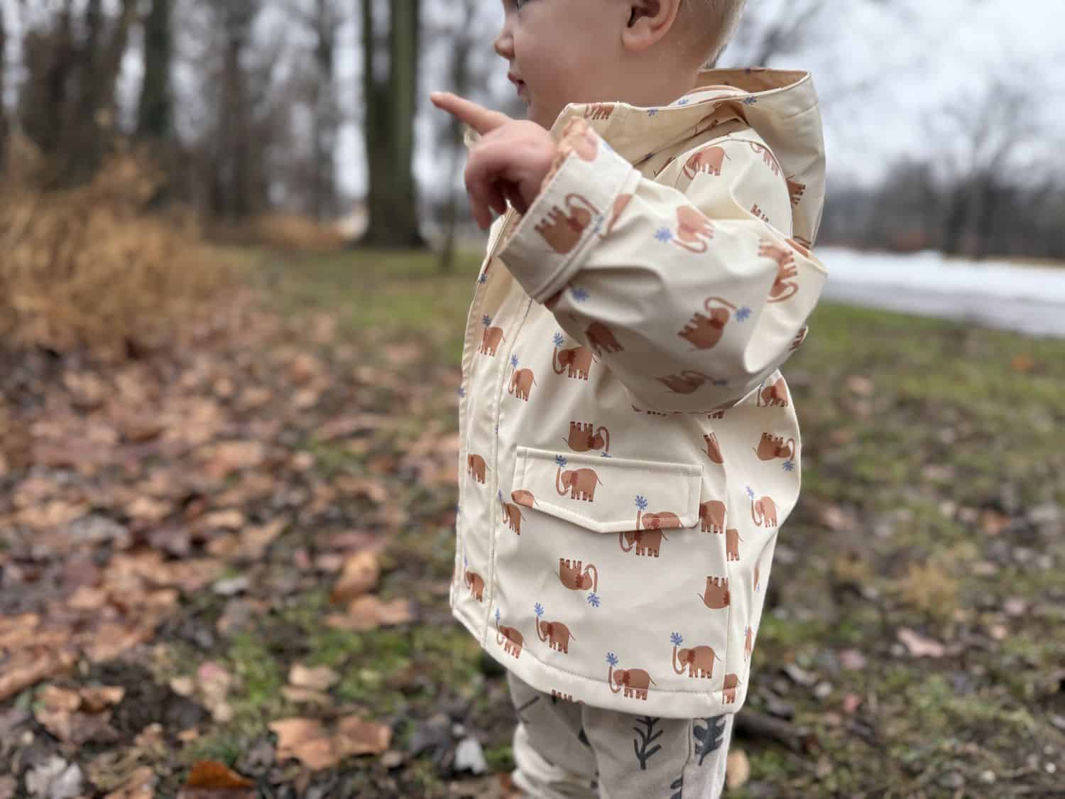 Side profile of toddler in navy Amazon Essentials Toddler Rain Jacket pointing at something, showing elephant print lining visible at cuff