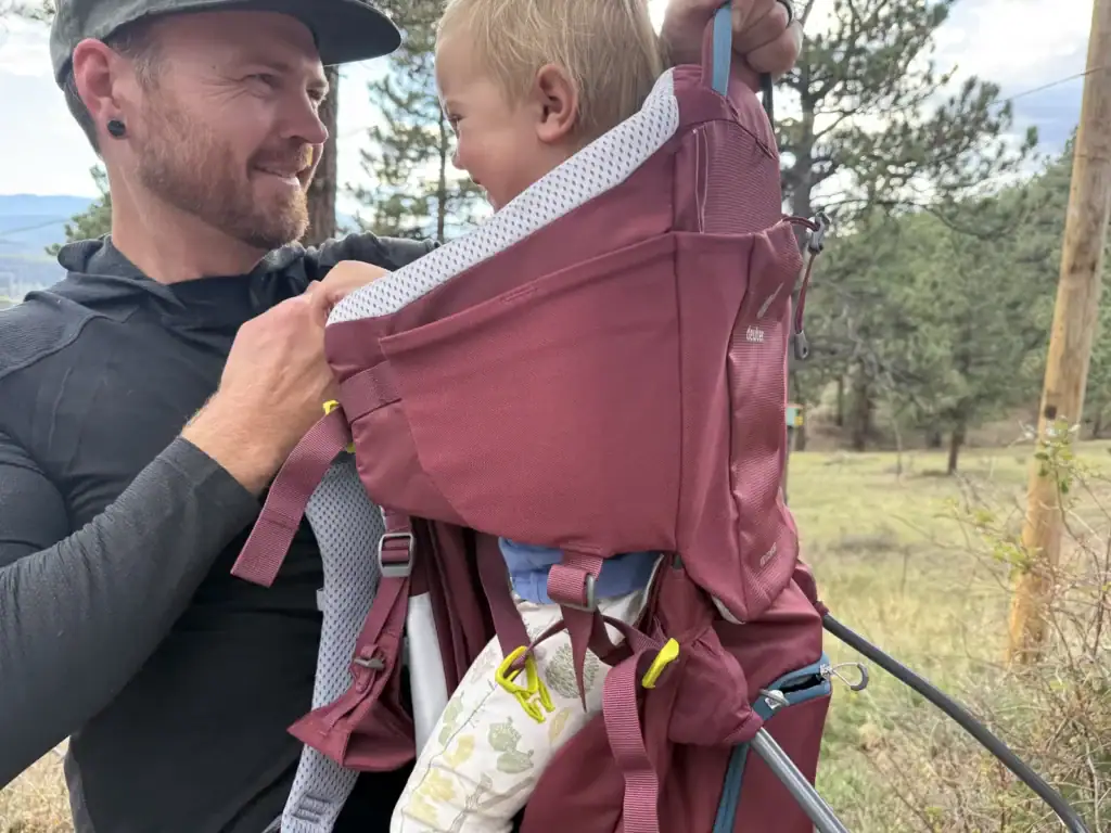 Adult adjusting the harness on the Deuter Kid Comfort child carrier with a toddler seated inside