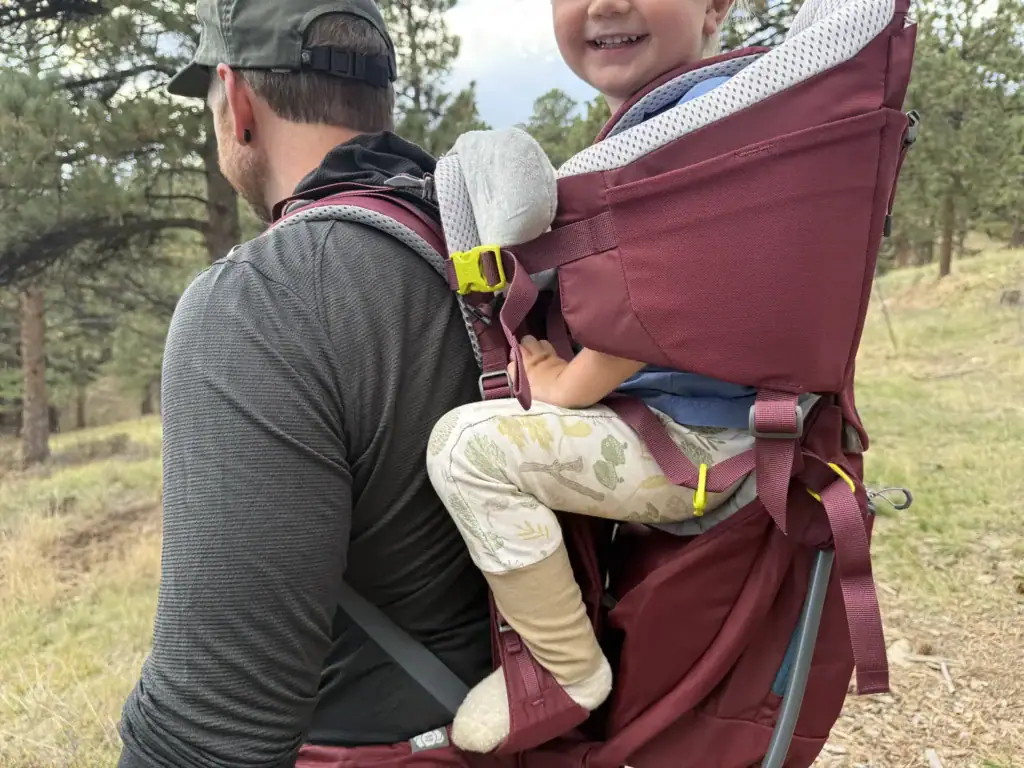 Dad hiking with a grinning toddler riding in the Deuter Kid Comfort child carrier