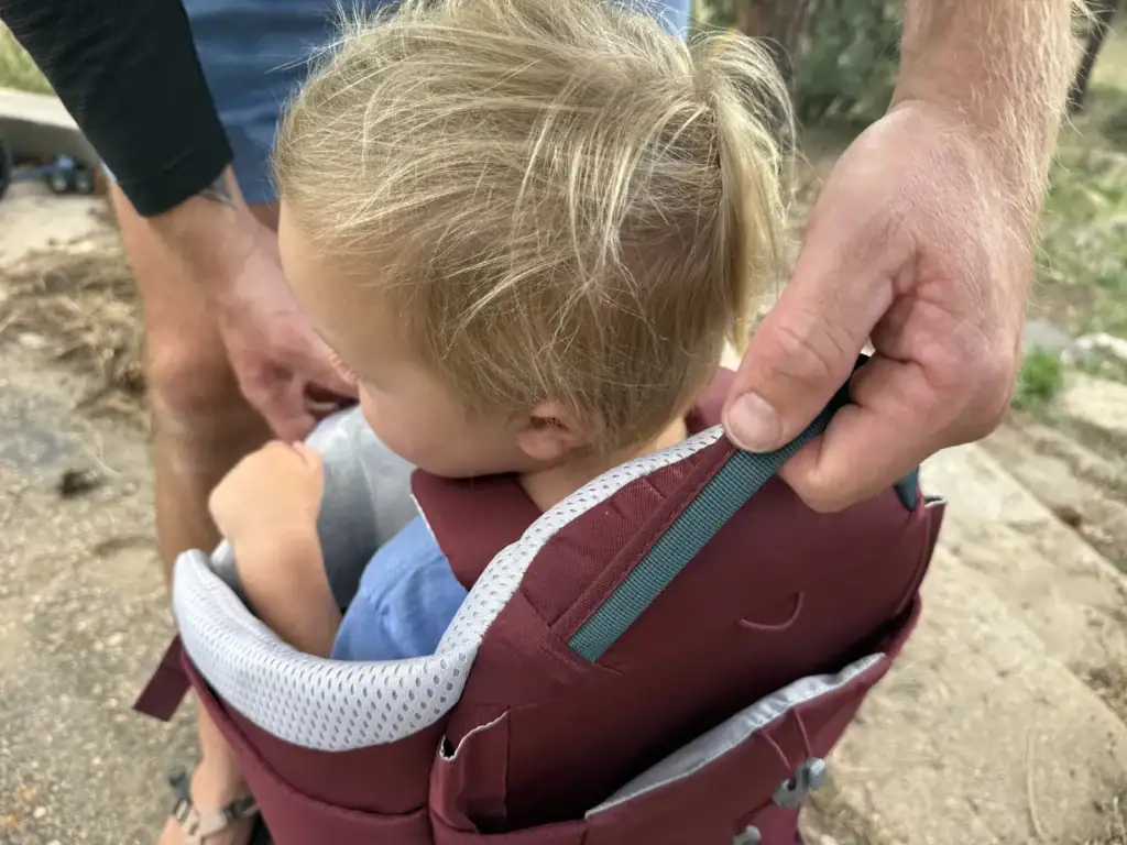 Adult unclipping the side entry on the Deuter Kid Comfort child carrier as a toddler climbs in