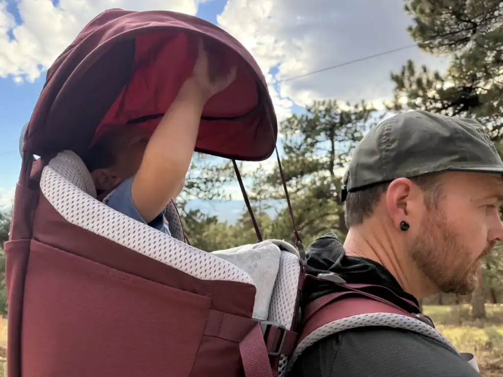 Sunshade deployed over a toddler riding in the Deuter Kid Comfort child carrier