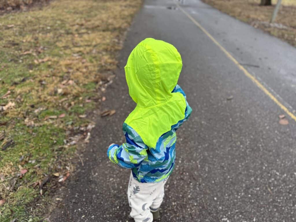 Eddie Bauer Toddler Rain Jacket with the bright yellow hood up on a toddler walking a paved path