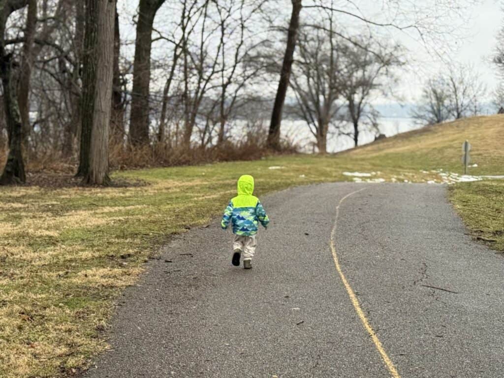 Toddler in the Eddie Bauer Toddler Rain Jacket walking a lakeside path in late winter