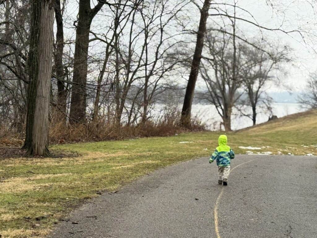 Toddler wearing the Eddie Bauer Toddler Rain Jacket walking away down a path by the water