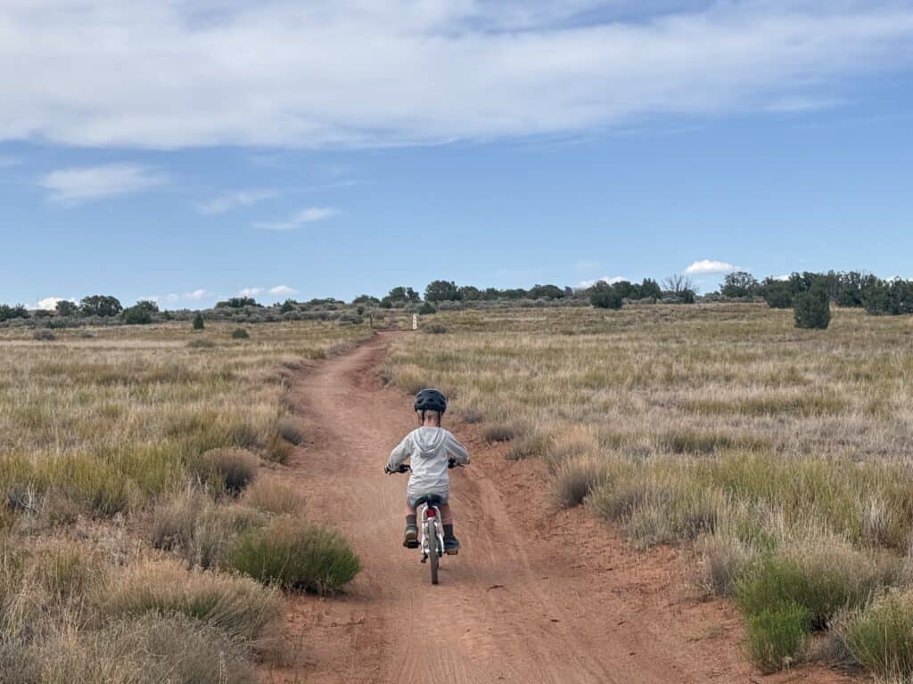 Kid riding a bike down a dirt road through grassland wearing Five Ten Freerider kids shoes