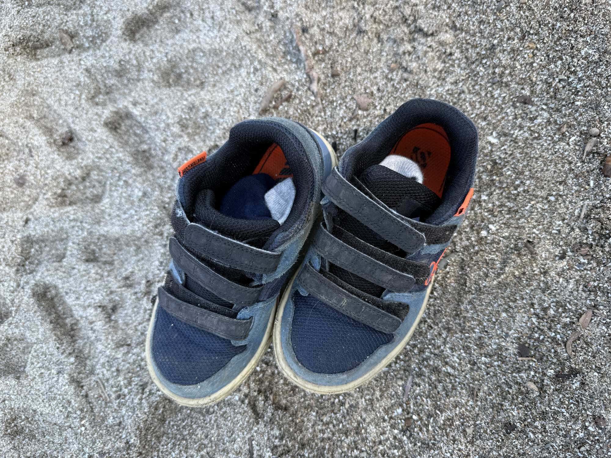 Pair of worn navy Five Ten Freerider kids shoes with three hook-and-loop straps on sand