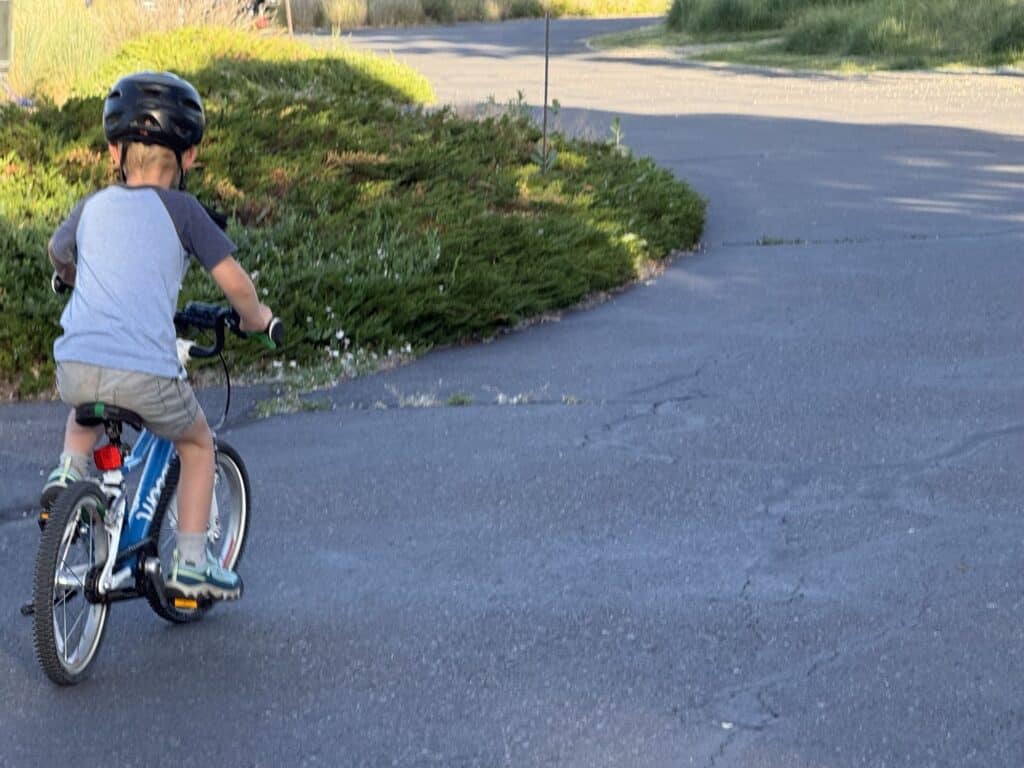 Kid in a helmet riding a bike on a paved path wearing KEEN Targhee IV Low Waterproof shoes