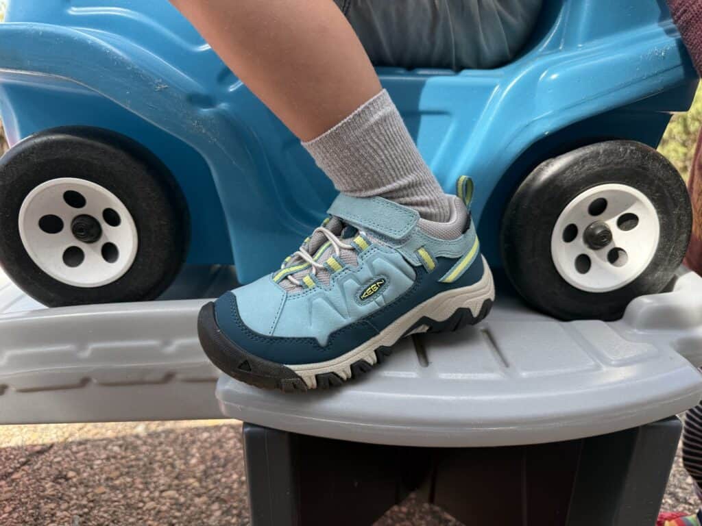 Kid foot in a KEEN Targhee IV Low Waterproof shoe resting on a toy car