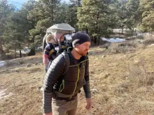 Dad hiking a sunny winter trail with a bundled toddler in the Kelty Journey PerfectFIT Elite child carrier